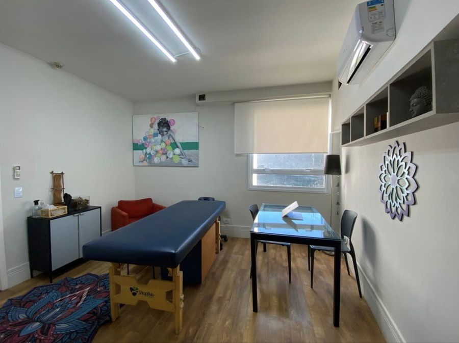 Sala ampla de atendimento, com maca, poltrona e mesa de avaliação.
